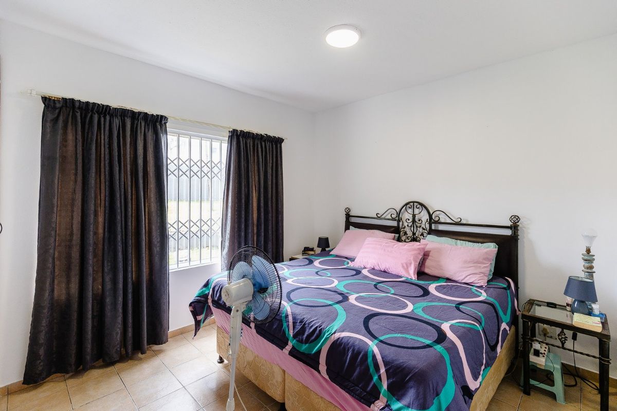 A functional bedroom featuring tiled flooring, a window with a security gate, and neutral wall finishes.