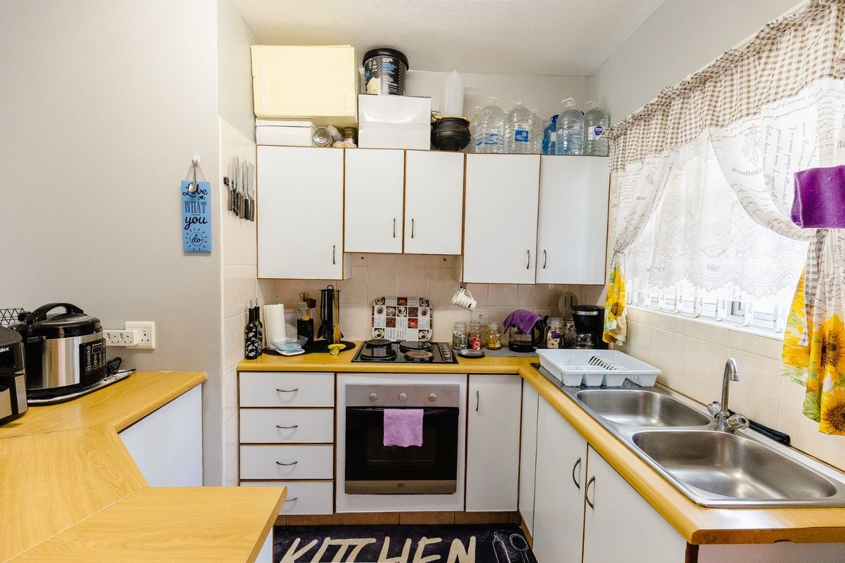 A functional kitchen featuring white cabinetry, laminate countertops, a double stainless steel sink, and a built-in oven with an electric hob.