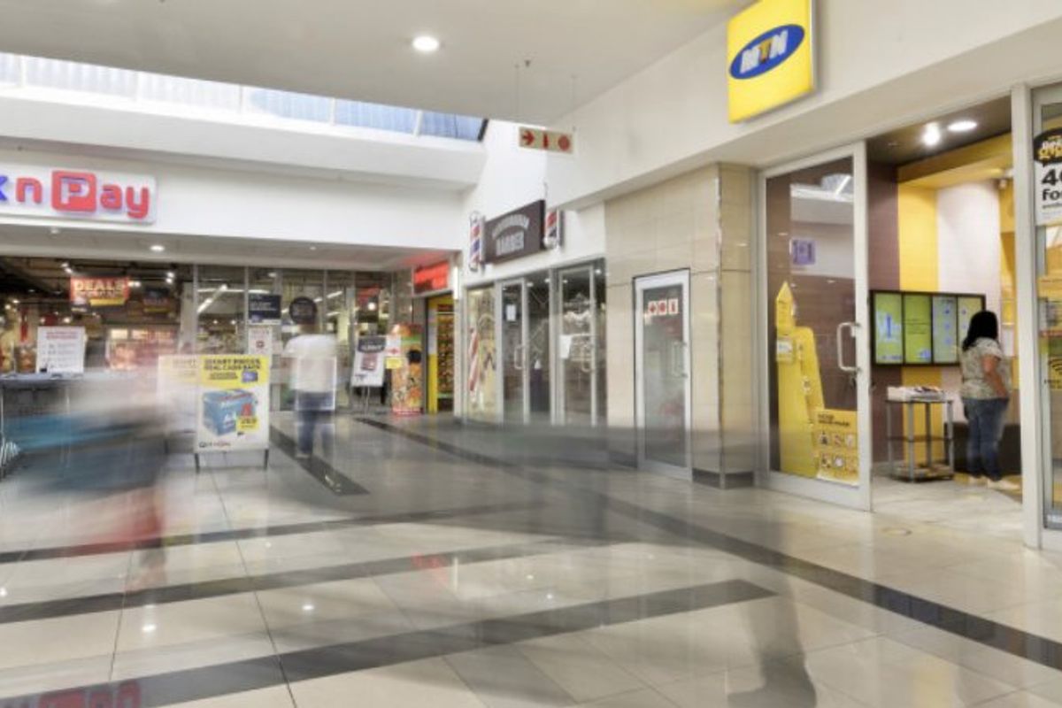 A well-maintained commercial shopping center hallway featuring polished tiled flooring, recessed lighting, and multiple glass-fronted retail storefronts.
