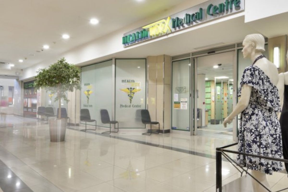 Commercial medical centre entrance featuring a glass storefront, automatic sliding doors, and polished tiled flooring within a shopping centre environment.