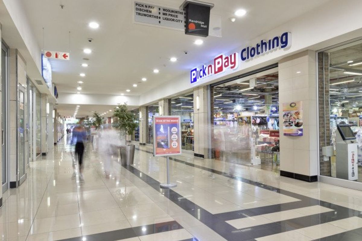 A well-maintained commercial shopping centre corridor featuring polished tiled flooring, recessed lighting, and clear glass storefronts for retail units.
