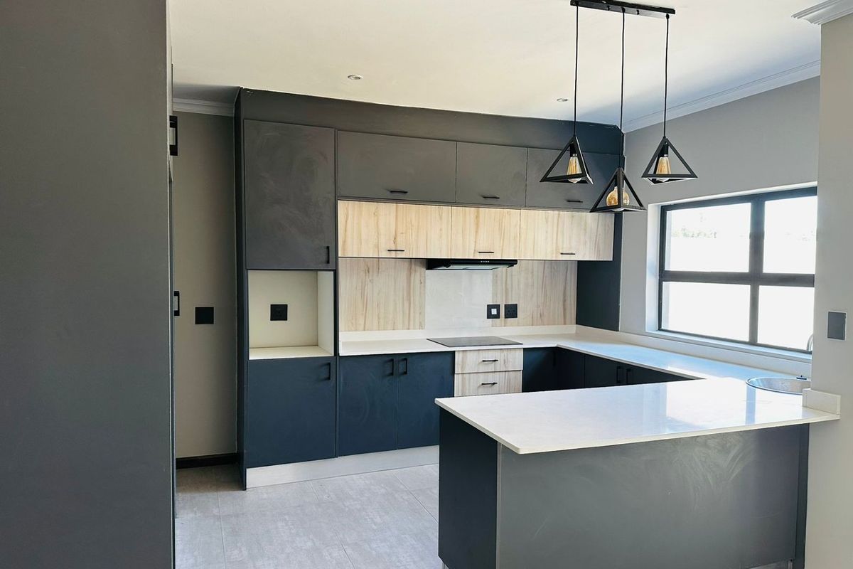 Modern kitchen featuring two-tone cabinetry, stone countertops, integrated hob, extractor fan, and contemporary pendant lighting in a clean, open-plan layout.