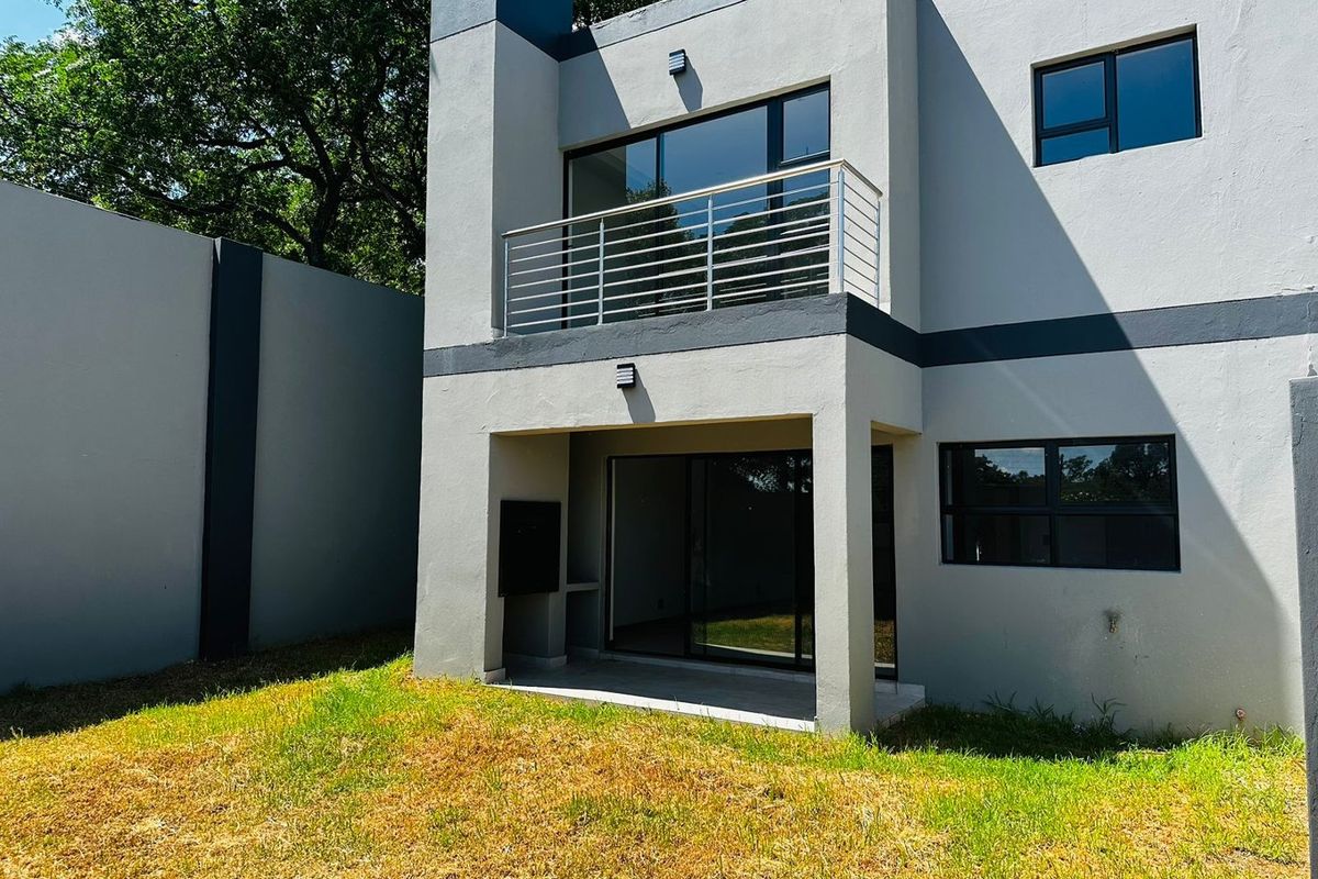 Rear view of the townhouse featuring a covered patio with built-in braai, a first-floor balcony with stainless steel balustrade, and a private garden area.