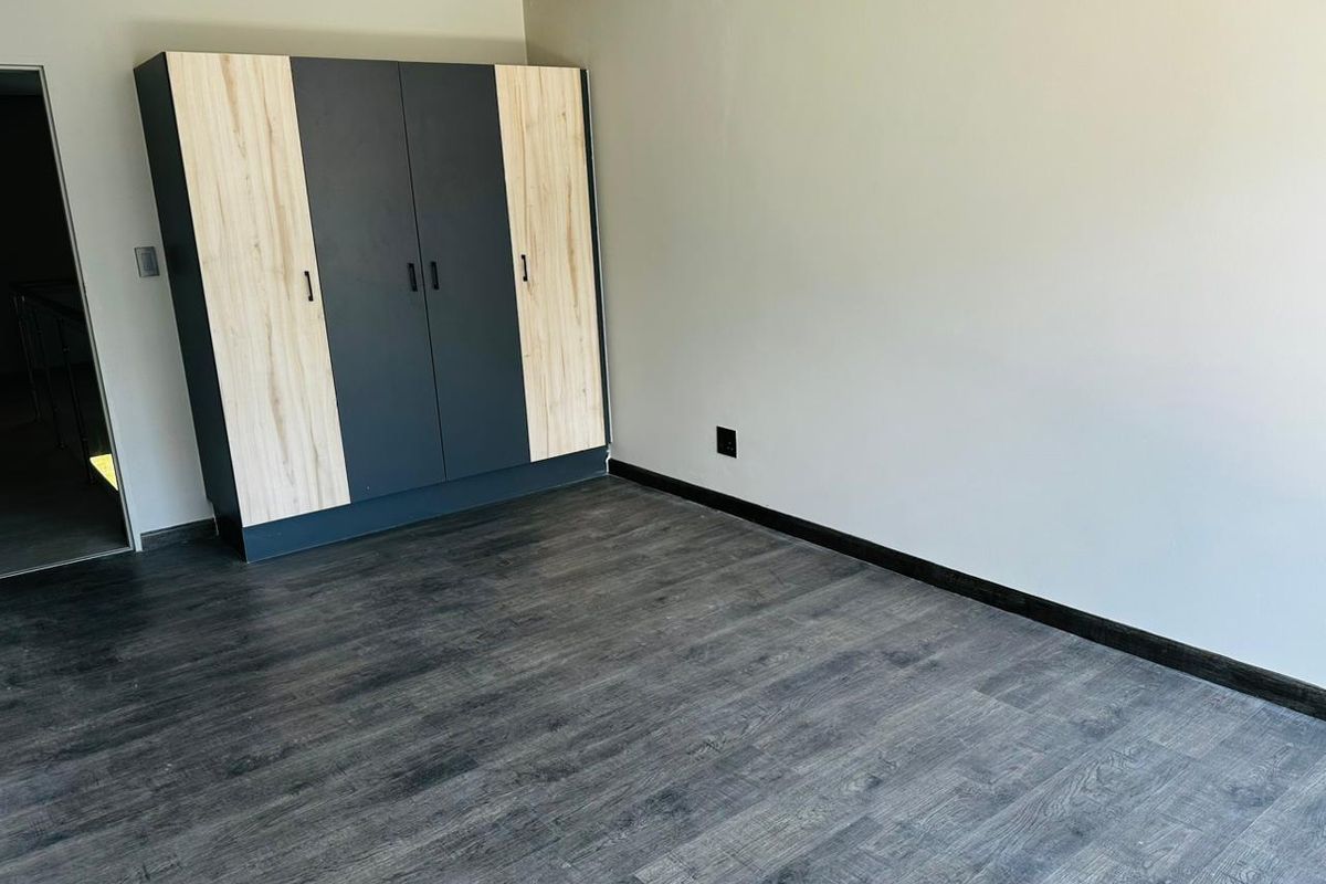 A clean, empty bedroom featuring modern laminate flooring and a contemporary two-tone built-in wardrobe.