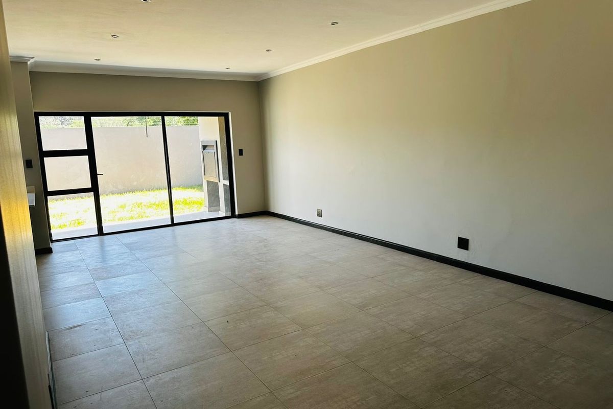 Spacious, empty living area featuring neutral tiled flooring, recessed downlighting, and large sliding glass doors providing access to the outdoor space.