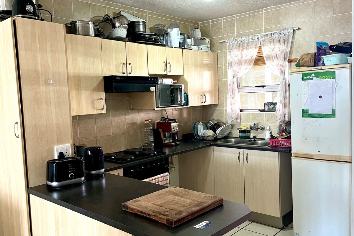 A functional kitchen featuring light wood-tone cabinetry, dark laminate countertops, a tiled backsplash, and a built-in hob with an extractor fan.