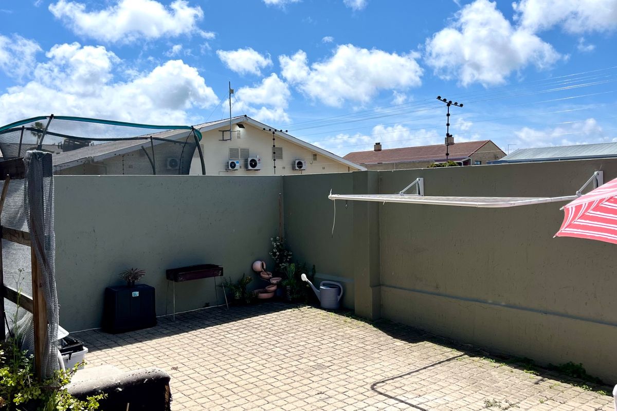 A private rear courtyard featuring paved flooring, a high boundary wall for privacy, and a wall-mounted clothesline.