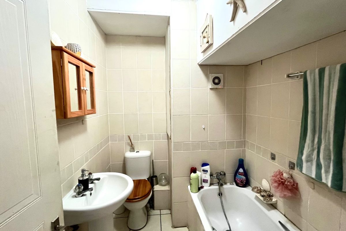 A compact bathroom featuring a pedestal basin, toilet, and bathtub with full-height wall tiling and integrated overhead storage.