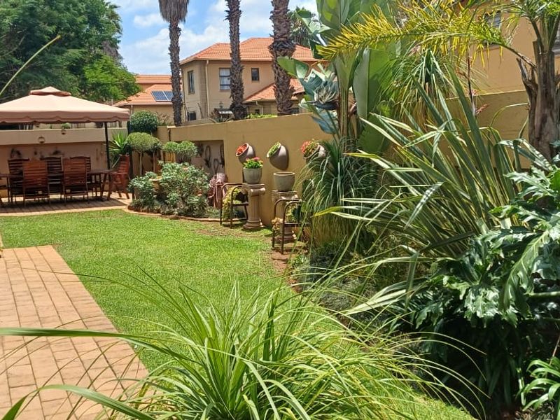 A well-maintained private garden featuring a paved walkway, lush lawn, and established perimeter boundary walls.
