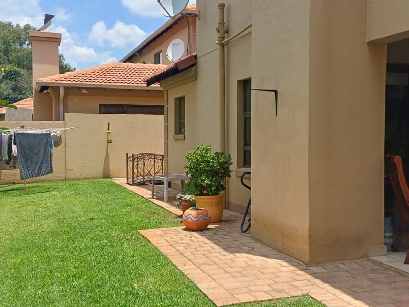 A rear garden view featuring a well-maintained lawn, a paved walkway, and a covered patio area attached to the main dwelling.