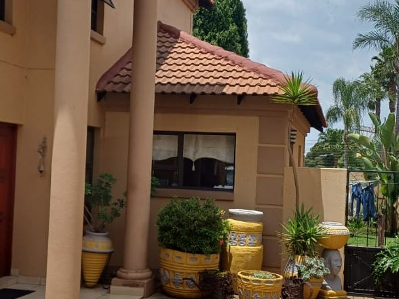 A covered patio area featuring classic columns, terracotta roof tiles, and paved flooring, providing a welcoming outdoor transition space.