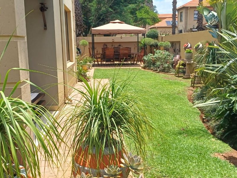 A well-maintained rear garden featuring a paved patio area, lush green lawn, and established perimeter boundary walls.