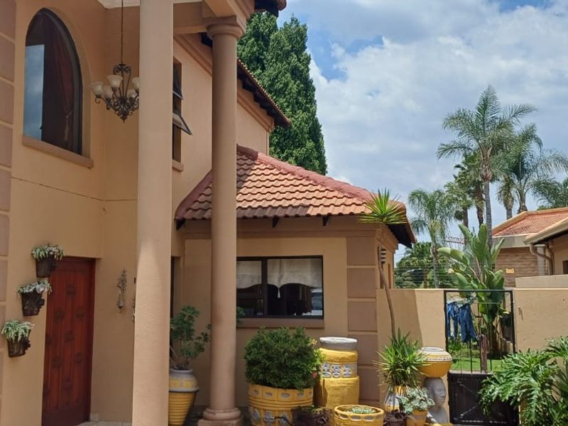 A view of the rear exterior facade featuring terracotta roof tiles, structural columns, and an arched window, leading to a private garden area.