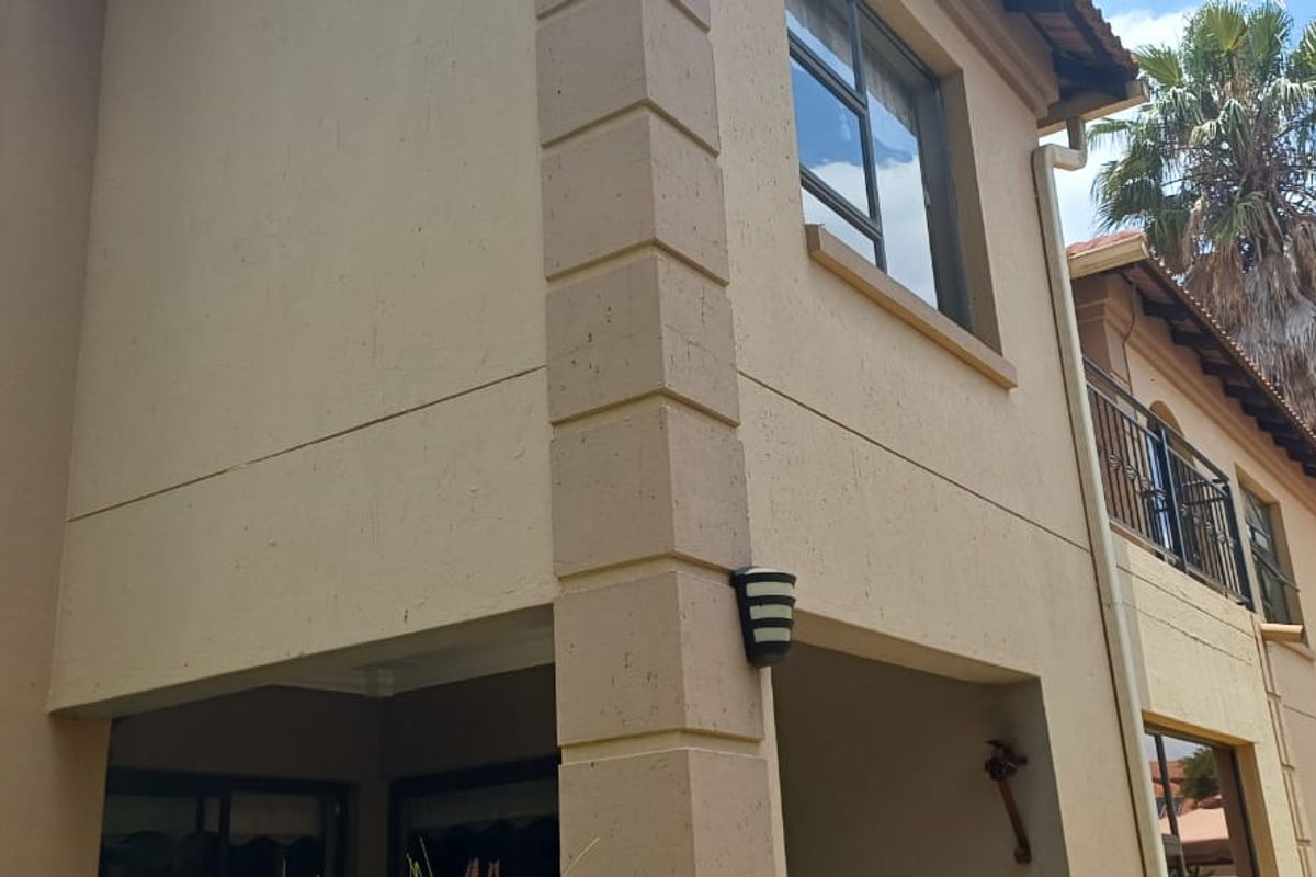 Rear elevation of a two-story house featuring a stucco facade, a balcony with wrought iron railings, and a tiled roof.