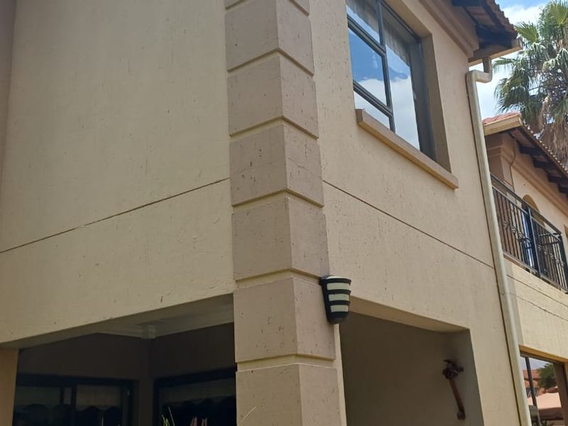 Rear elevation of a two-story house featuring a stucco facade, a balcony with wrought iron railings, and a tiled roof.