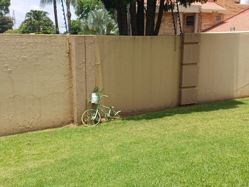 A rear garden area featuring a perimeter wall with integrated electric fencing and a well-maintained lawn.