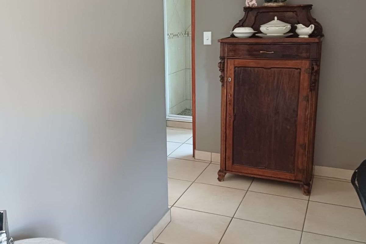 A bedroom featuring neutral wall tones, tiled flooring, and built-in cupboards, with an adjacent view into a tiled bathroom area.