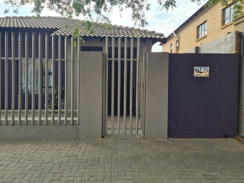 Front exterior view of the property featuring a tiled roof, secure metal fencing, a gated entrance, and a paved driveway area.