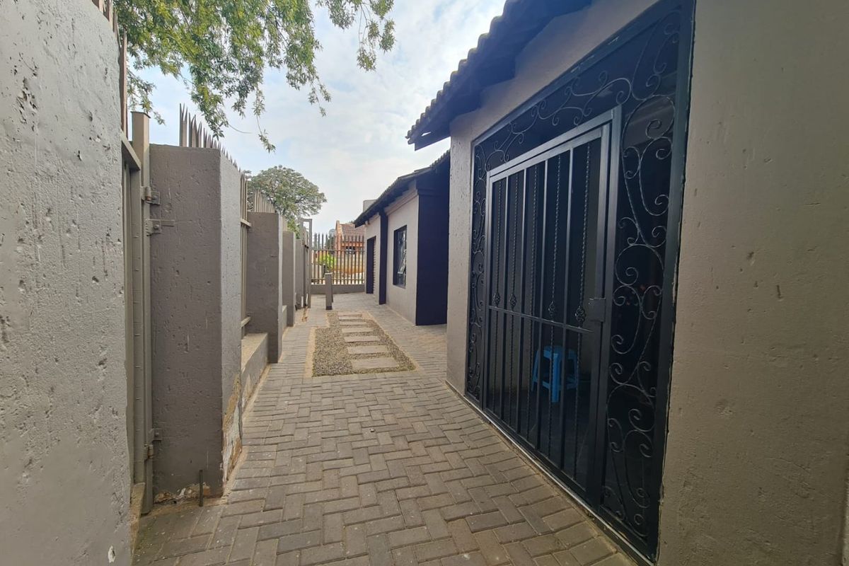 A paved side walkway featuring a secure metal gate, perimeter walling, and a gravel path leading along the side of the house.