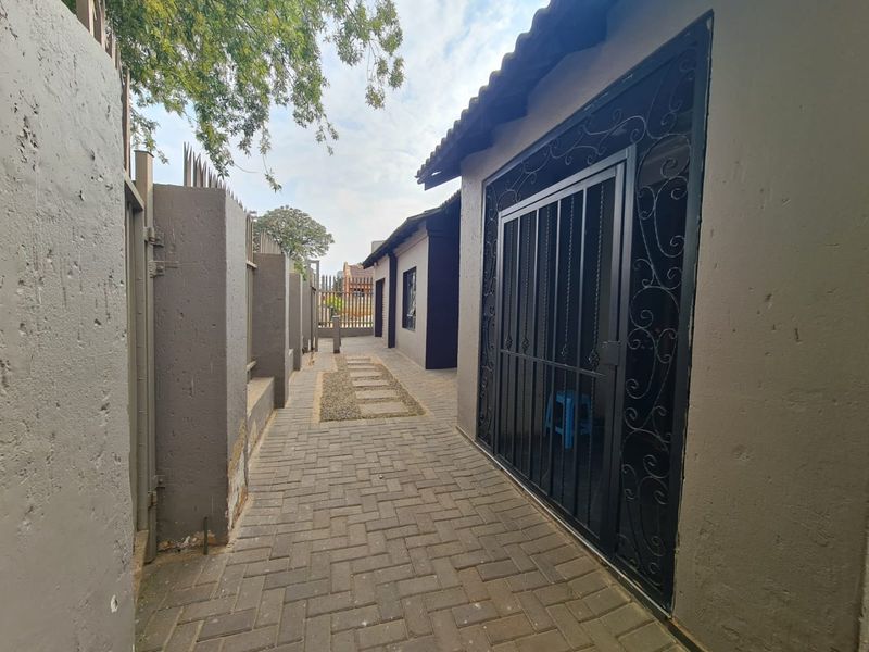 A paved side walkway featuring a secure metal gate, perimeter walling, and a gravel path leading along the side of the house.