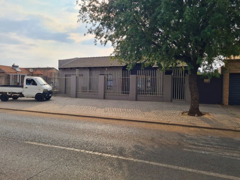 Front exterior view of the property featuring a tiled roof, secure perimeter fencing, and a paved driveway area.