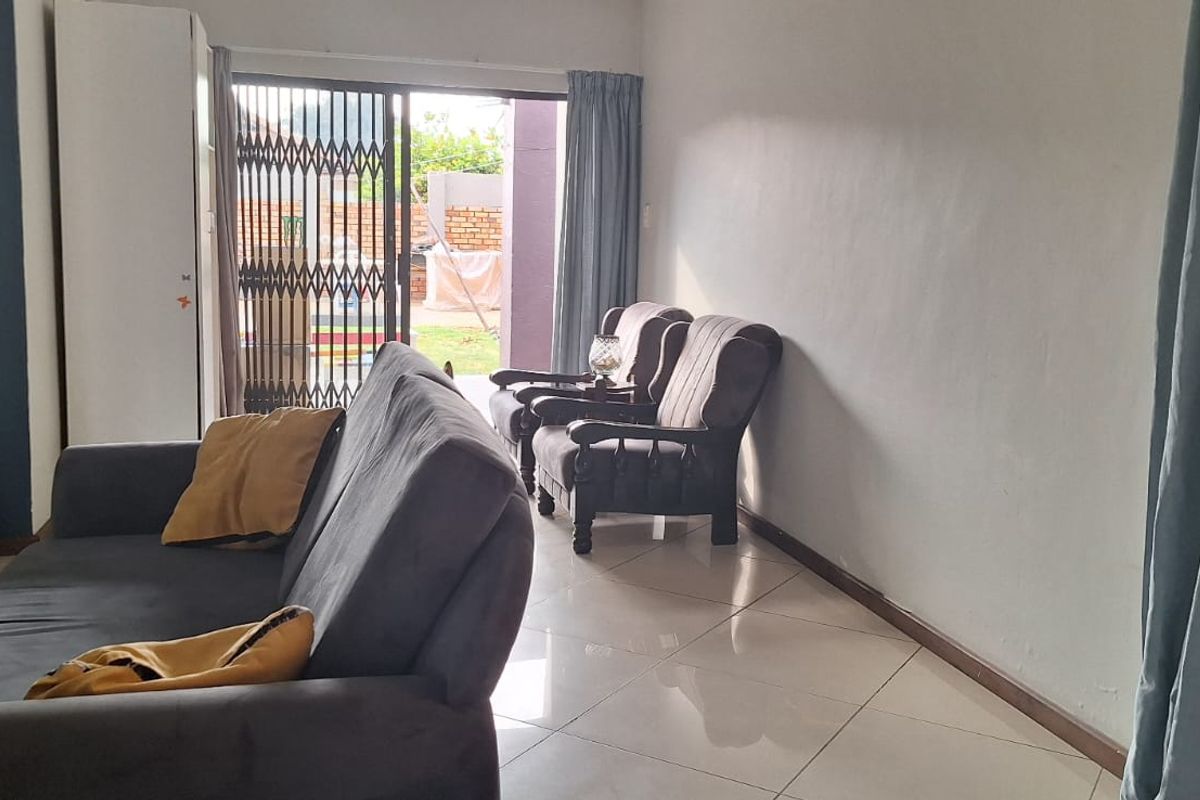 A living room featuring tiled flooring and a sliding glass door with a security gate, providing direct access to the outdoor area.