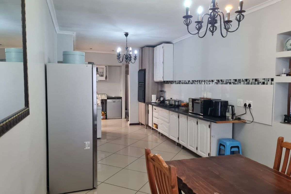 A functional kitchen featuring white cabinetry, dark countertops, mosaic tile backsplash, and tiled flooring, with an adjacent scullery area visible.