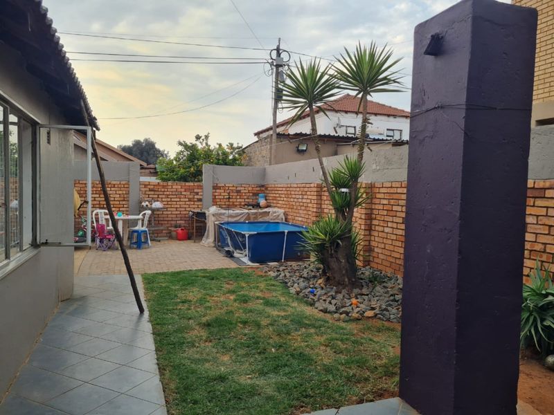 Rear garden area featuring a paved patio, brick boundary walls, and a small lawn section with established landscaping.