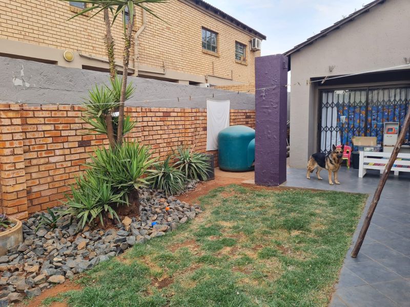 A rear garden area featuring a tiled patio, brick boundary wall, and landscaped garden bed with established plants.