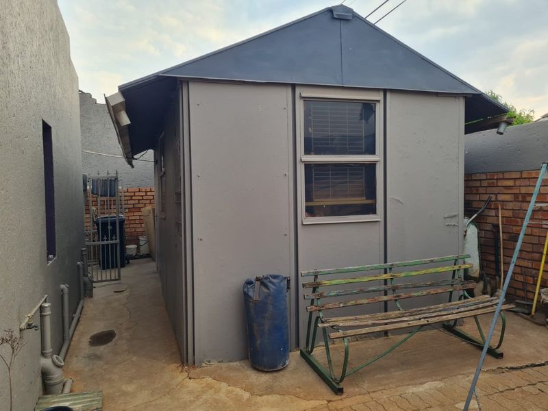 Rear exterior view of a detached outbuilding featuring a metal roof, sliding window, and concrete paved area with brick boundary walls.