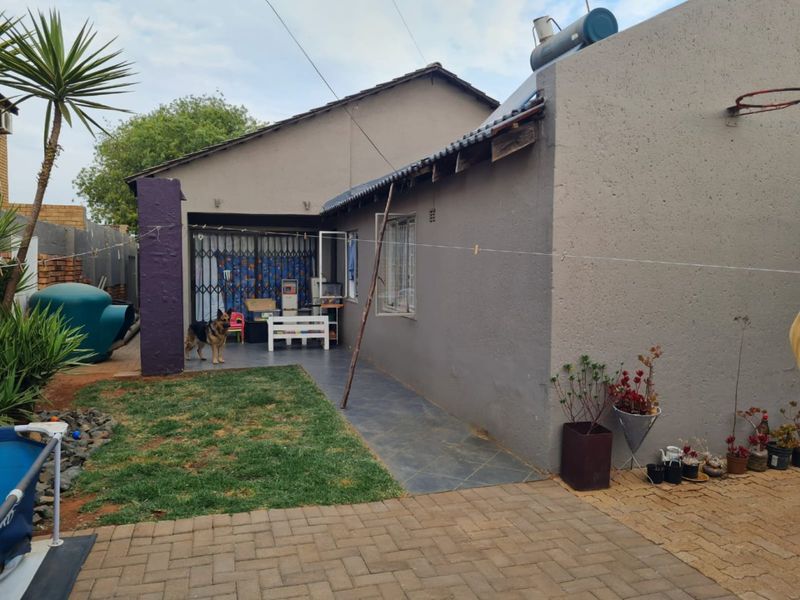 Rear exterior view of the house featuring a paved patio area, solar water heater, and garden space with visible maintenance required on roof eaves.
