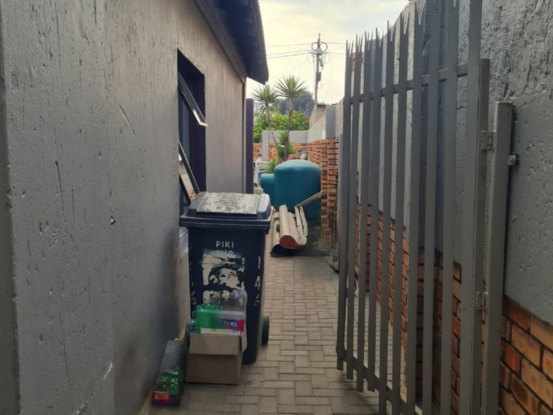 A narrow side passage featuring paved flooring, a metal security gate, and brick boundary walls, providing access to the rear of the property.