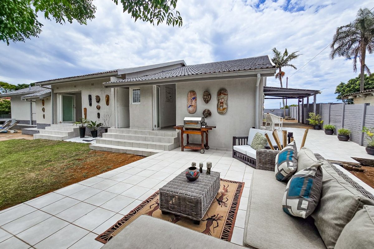 A spacious rear exterior featuring a large tiled patio area, concrete steps leading to the house entrance, and a well-maintained garden space.