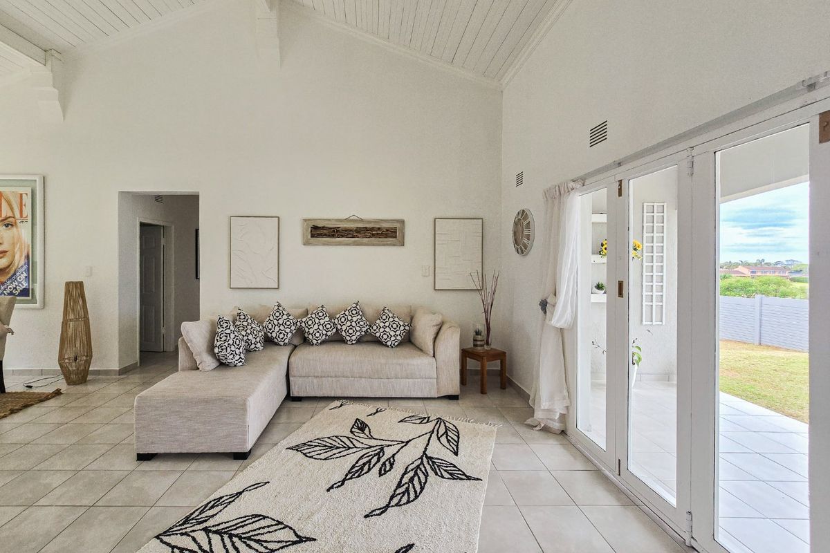 Spacious living room featuring vaulted ceilings with exposed rafters, neutral tiled flooring, and large glass doors providing seamless access to the outdoor patio area.