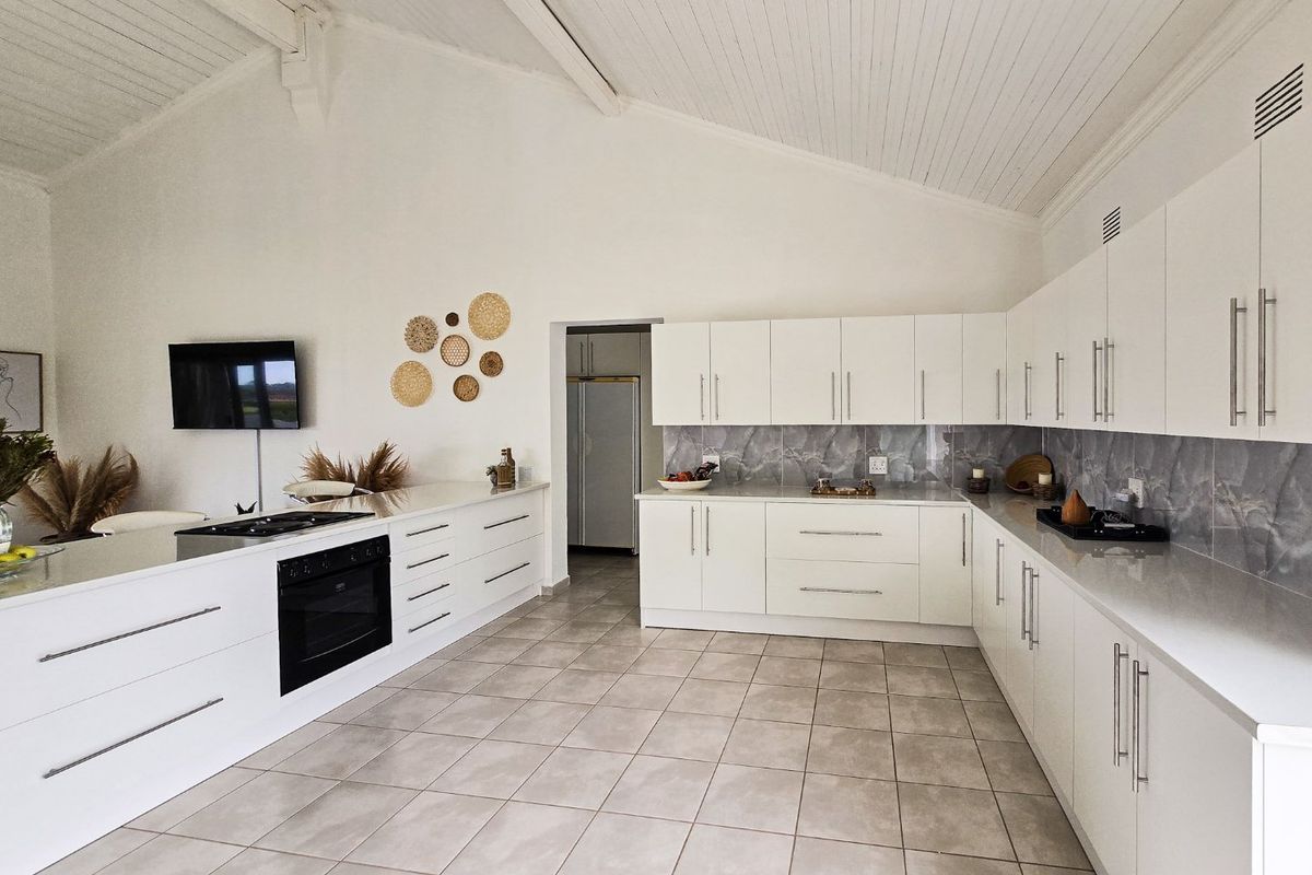 Modern, spacious kitchen featuring white cabinetry, stone countertops, a built-in oven, gas hob, and a high vaulted ceiling with tiled flooring.