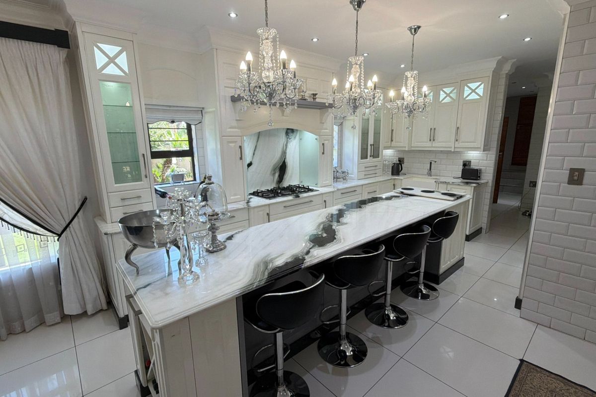 A high-end kitchen featuring a large marble-topped island, custom cabinetry, subway tile backsplash, and elegant crystal chandeliers.