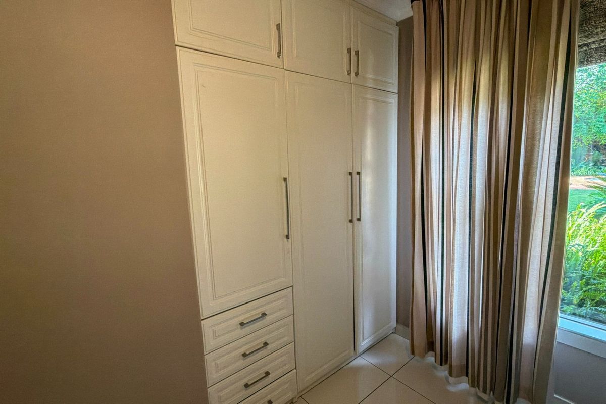 A bright bedroom featuring ample built-in cupboard storage and neutral tiled flooring, offering a clean and functional space.