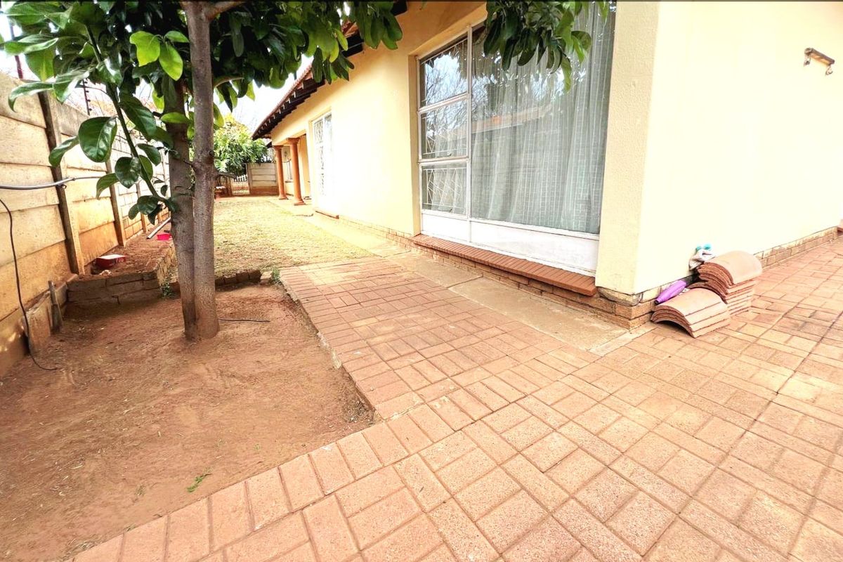 Rear exterior view featuring a paved patio area, sliding glass doors with security gates, and a garden space enclosed by a boundary wall.