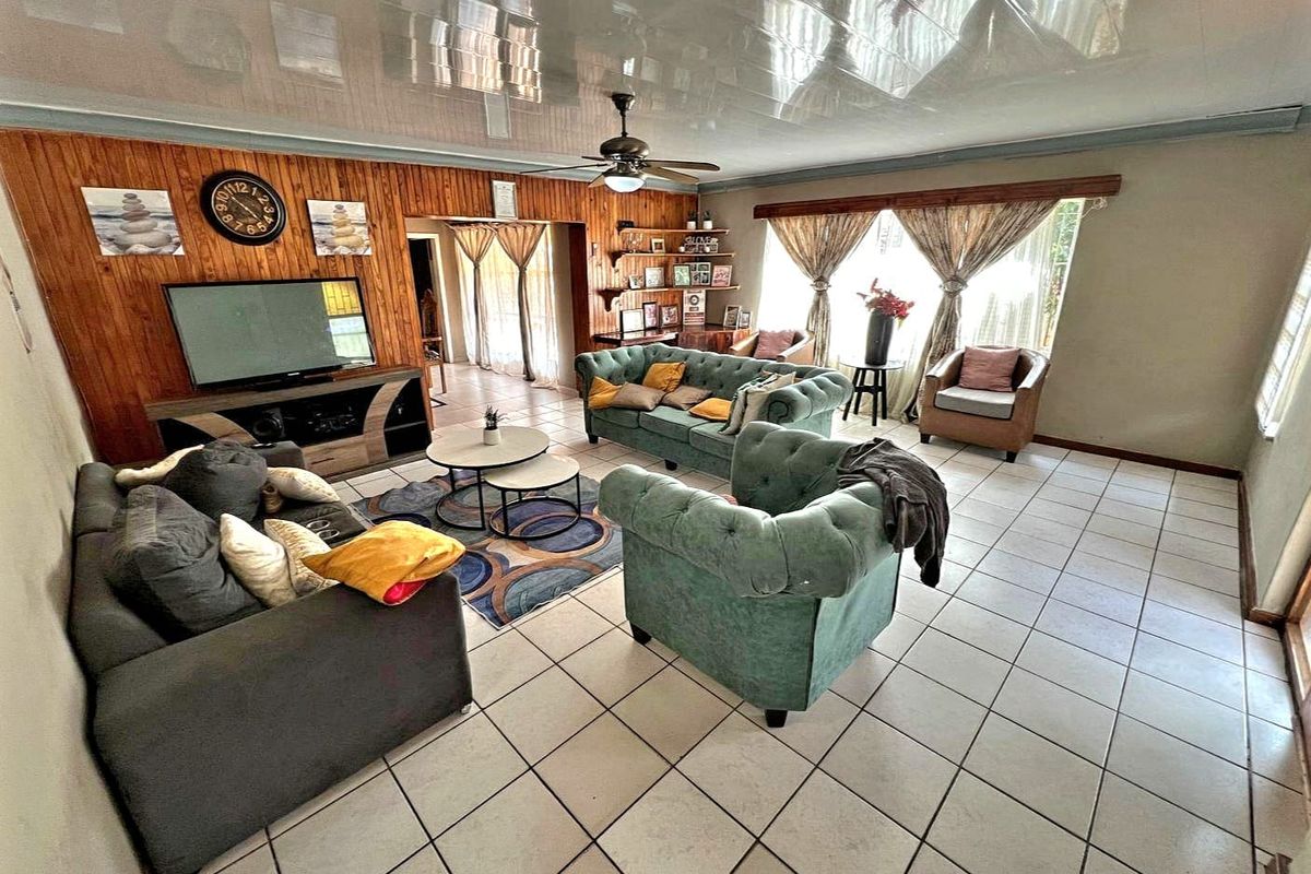 Spacious living room featuring wood-paneled accent wall, glossy ceiling finish, ceiling fan, and neutral tiled flooring throughout.