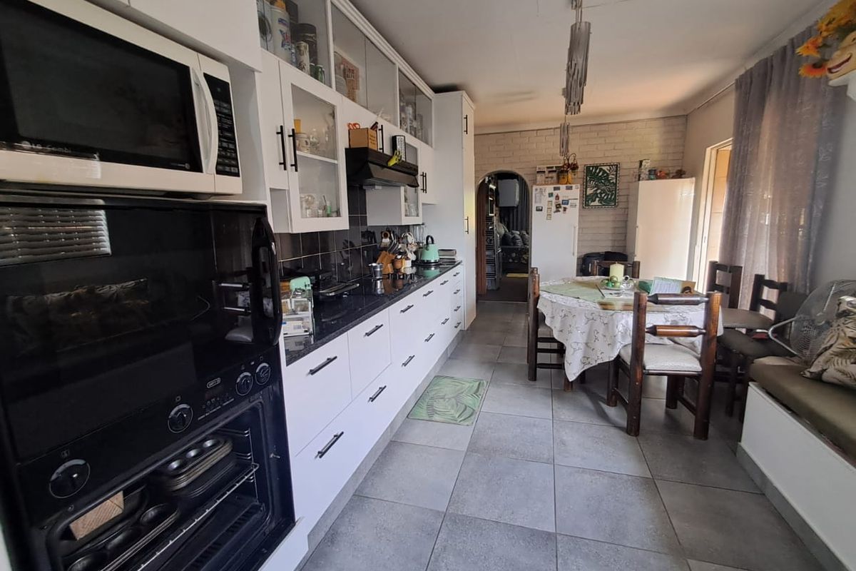 A functional kitchen featuring white cabinetry, dark stone countertops, built-in oven and microwave, and tiled flooring, with an integrated dining area.