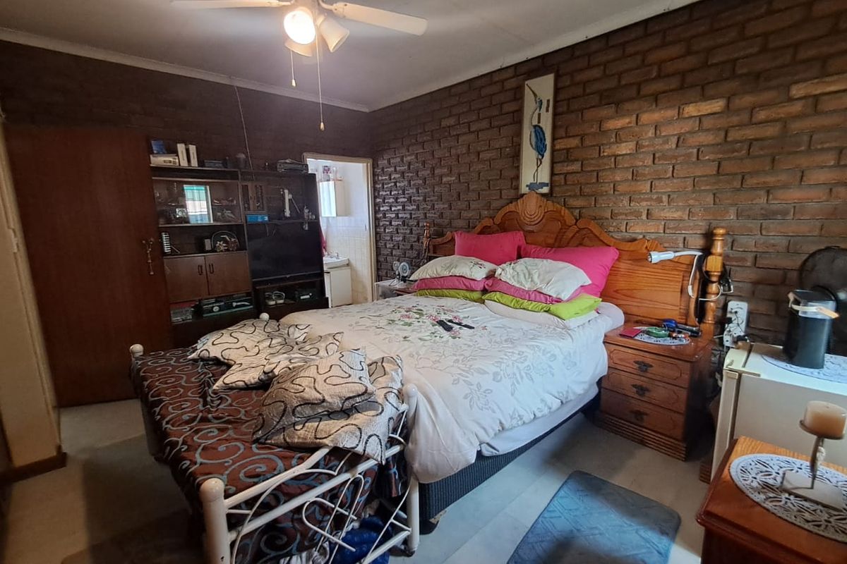A bedroom featuring an exposed brick feature wall, tiled flooring, and a ceiling fan, offering a rustic aesthetic with potential for modern updates.