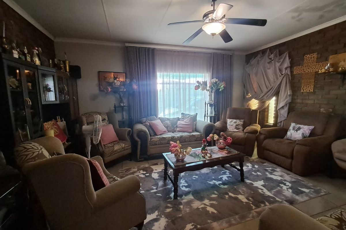 A cozy living room featuring exposed brick walls, tiled flooring, and a central ceiling fan, with visible signs of ceiling water damage.