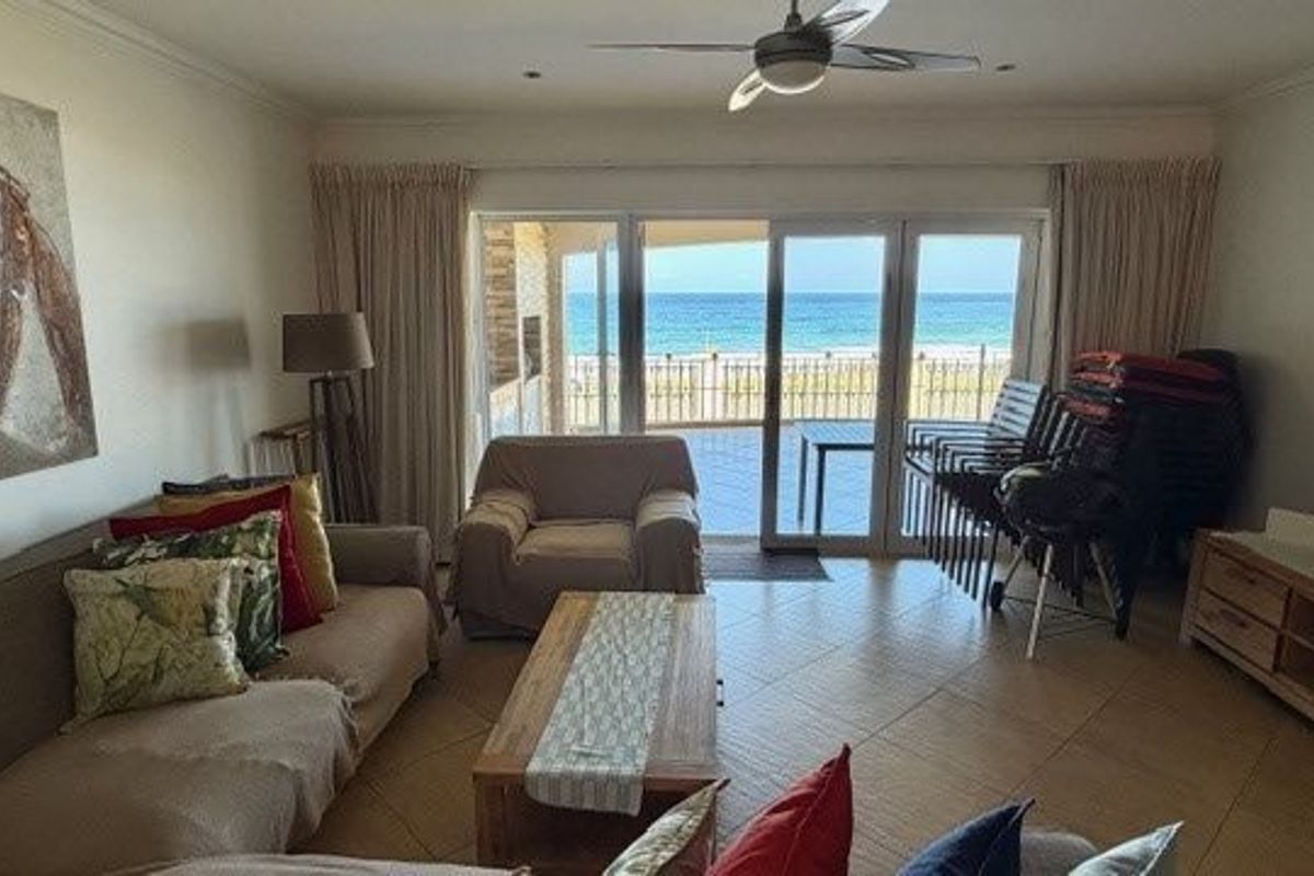 Spacious living room featuring tiled flooring, a ceiling fan, and large sliding glass doors that open to a scenic ocean view.