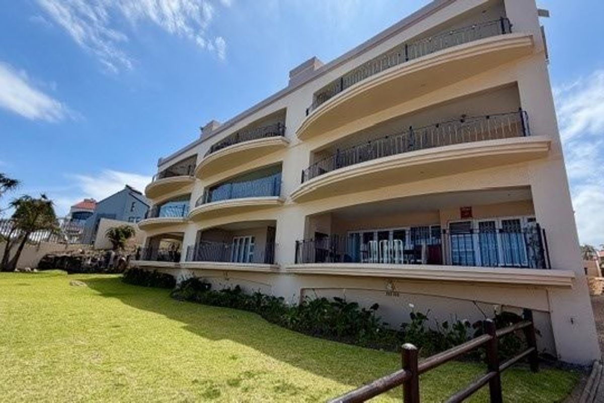 A view of the rear elevation of the apartment building, featuring multiple levels of balconies with wrought iron railings and a well-maintained lawn.