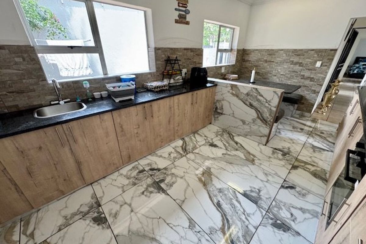 Modern kitchen featuring stone-look floor tiles, laminate cabinetry, granite countertops, and a built-in breakfast bar with a tiled backsplash.