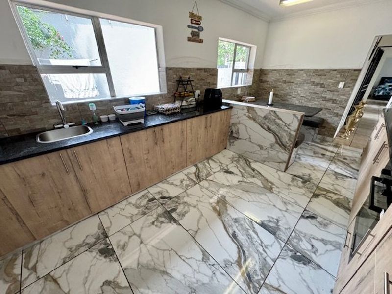 Modern kitchen featuring stone-look floor tiles, laminate cabinetry, granite countertops, and a built-in breakfast bar with a tiled backsplash.
