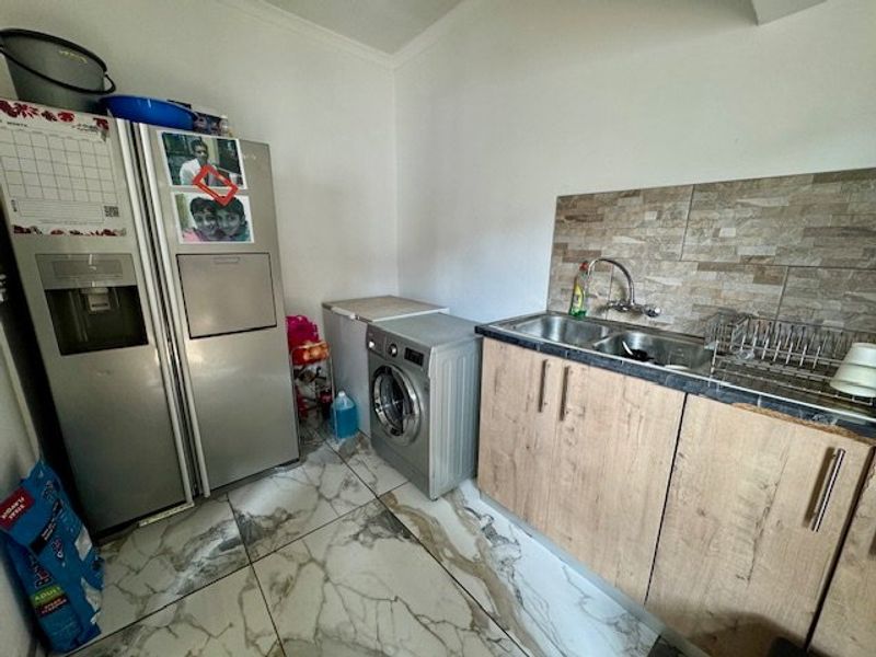A functional laundry area featuring marble-look floor tiles, laminate cabinetry, and a double bowl sink with a tiled splashback.