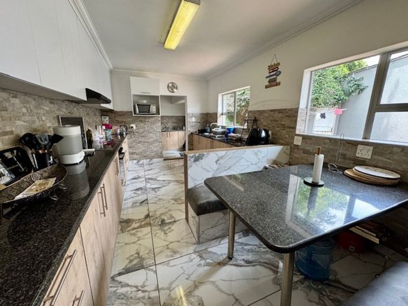 A functional kitchen featuring granite countertops, stone tile backsplash, marble-look flooring, and a built-in breakfast nook with integrated cabinetry.