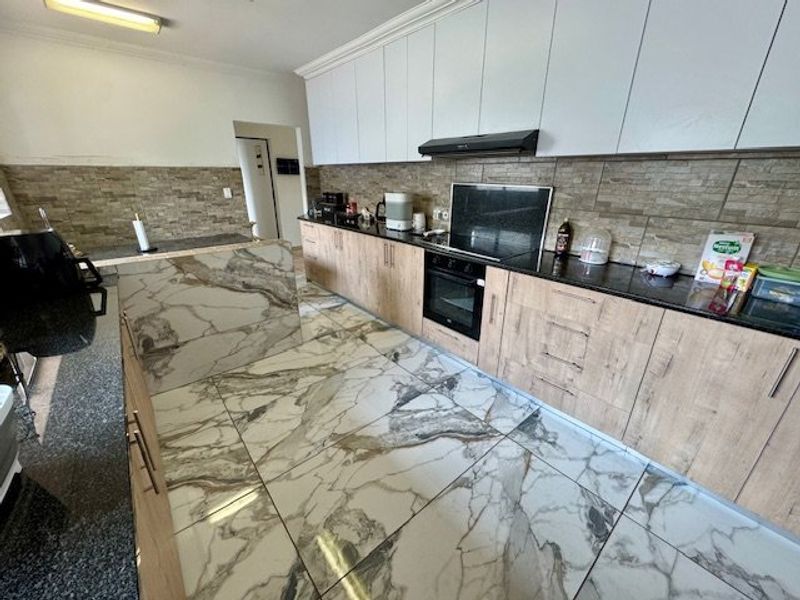 Modern kitchen featuring wood-finish cabinetry, granite countertops, stone-look floor tiles, and integrated appliances including an oven and extractor fan.