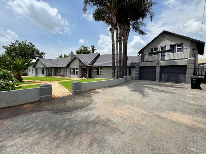 Front exterior view of a spacious house featuring a double garage, paved driveway, tiled roof, and a balcony above the garage area.